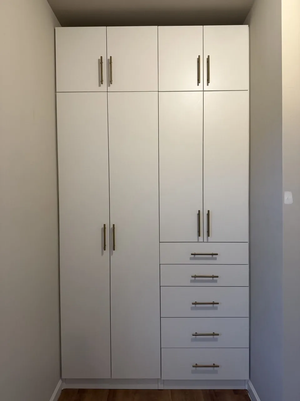 Tall white reach-in closet with a five-drawer stack and gold pulls