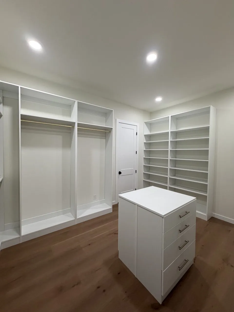 Bright white walk-in closet with a centre island and shoe shelving